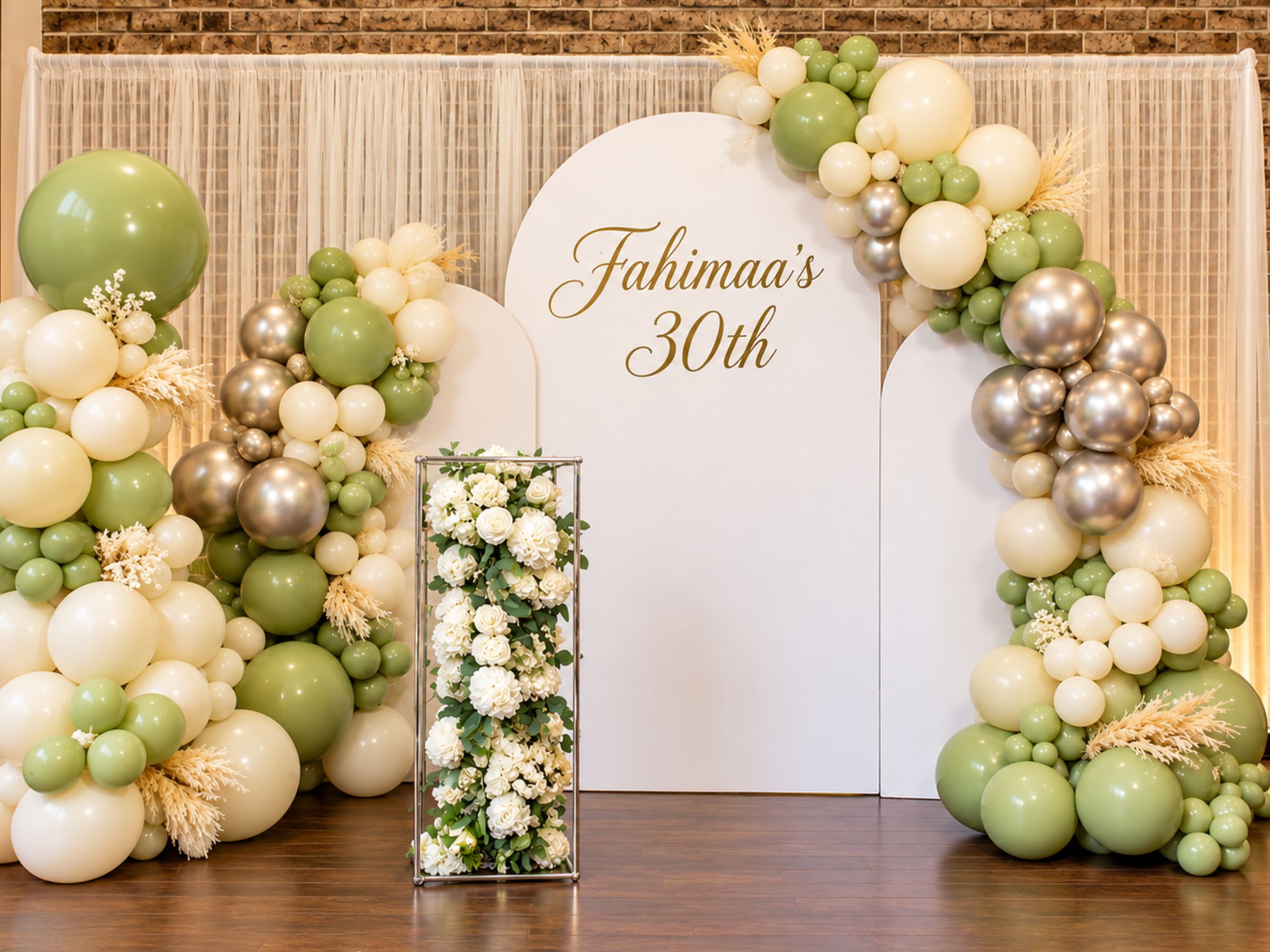 Green, white and gold balloon display with flowers and a backdrop.