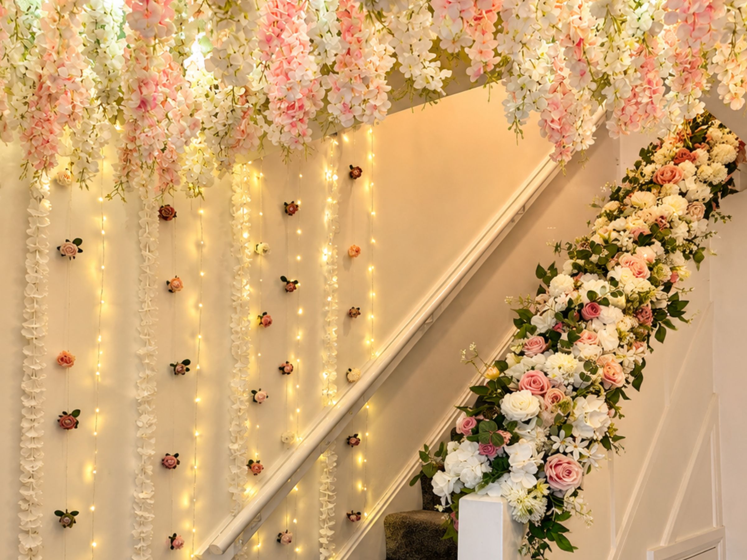 Staircase decorated with white and pink flowers and warm string lights.